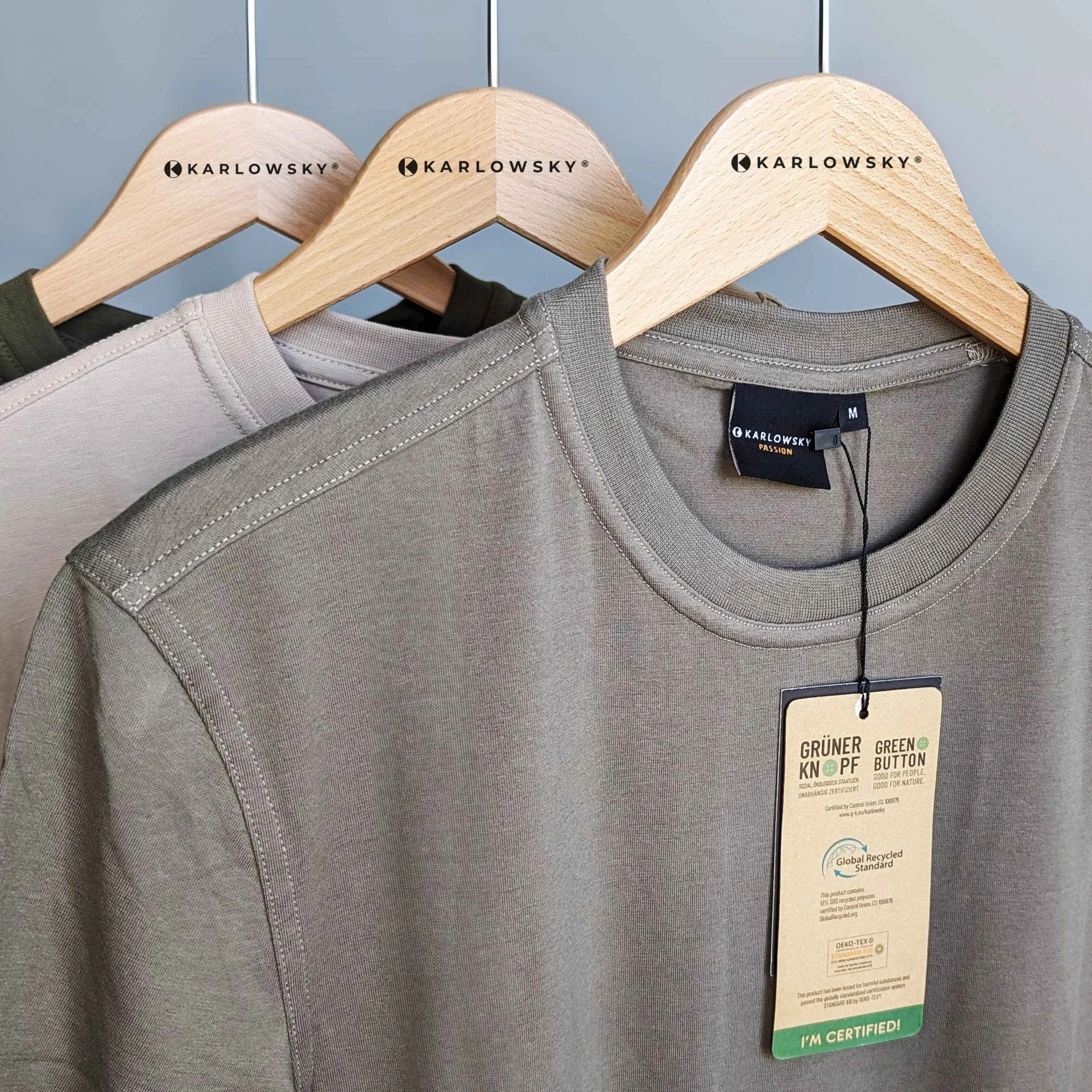 Karlowsky Fashion T-Shirts auf Kleiderbügeln Hochformat Drei Kleiderbügel von Karlowsky mit drei T-Shirts von Karlowsky. Aus dem einen T-Shirt hängt ein Schild mit der Aufschrift: "I´m certified".