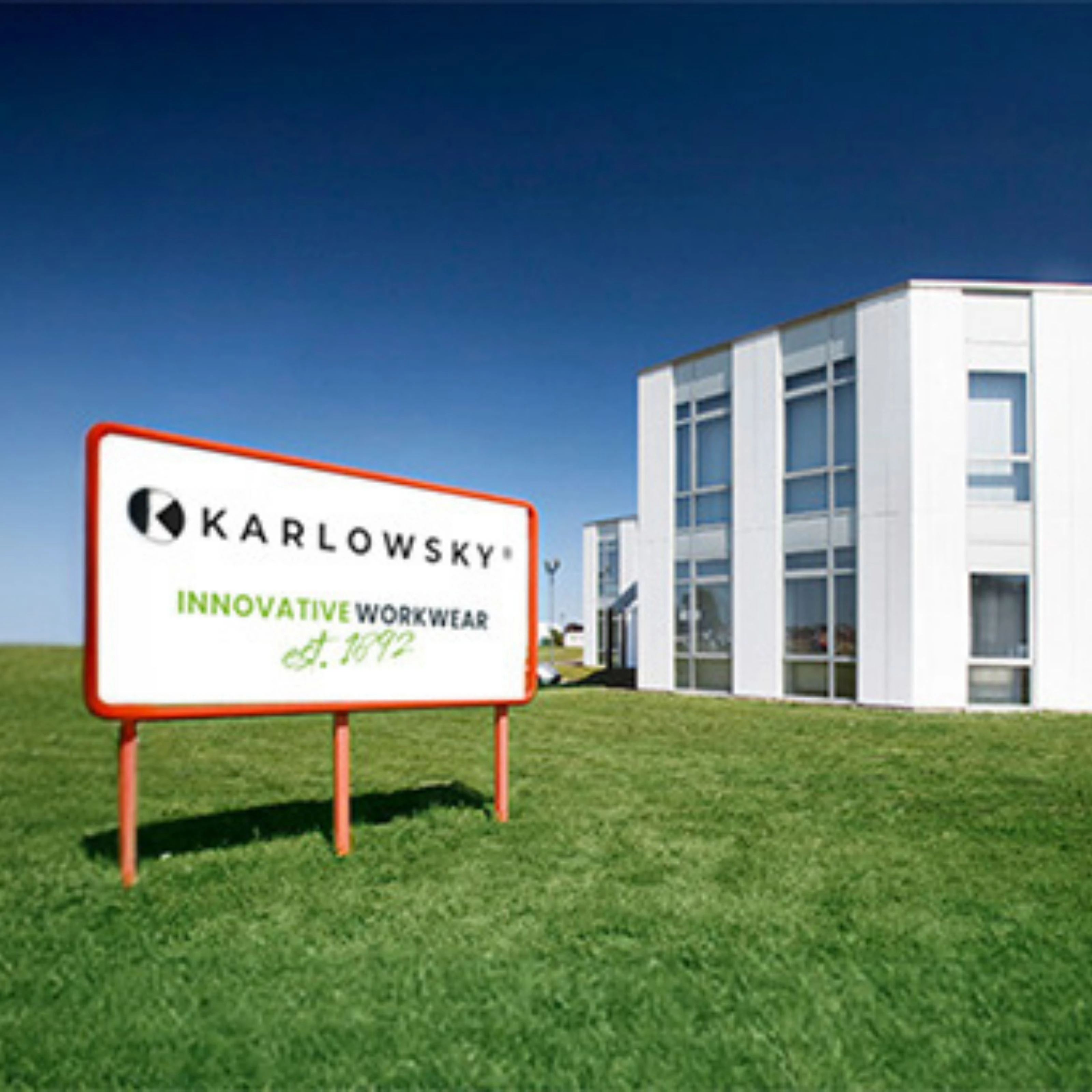 Karlowsky Fashion GmbH Unternehmen von Außen Hochformat Schild mit Schriftzug: "Karlowsky - innovative Workwear est 1892" steht vor dem Firmengebäude.